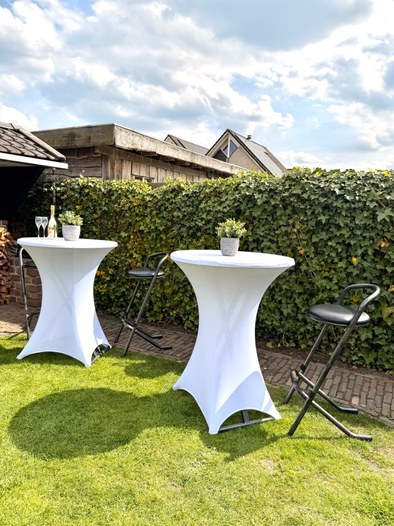 Twee statafels met witte rokken en barkrukken in de tuin